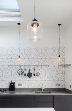 a kitchen with black cabinets and white tile backsplash, hanging lights over the sink