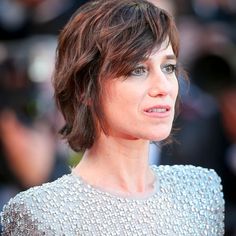 a woman with short hair wearing a silver dress and looking off to the side while standing in front of photographers