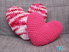 two crocheted hearts sitting on top of a gray couch next to each other