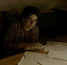 a man sitting at a table reading a book in front of some papers on top of it