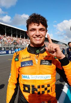 a man in an orange racing suit is giving the peace sign with his right hand