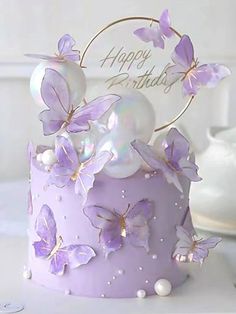 a birthday cake with purple butterflies and pearls on the top is decorated with a happy birthday sign