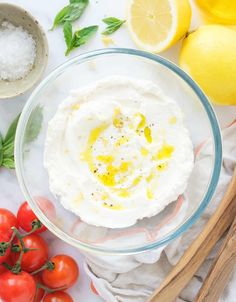 a glass bowl filled with whipped cream surrounded by tomatoes, lemons and basil leaves