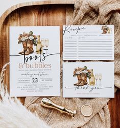 the wedding stationery is laid out on top of a wooden tray with wine glasses