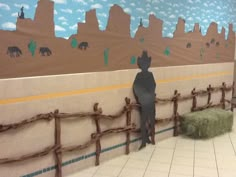 a person standing next to a fence with animals painted on the wall behind it and grass in front of them