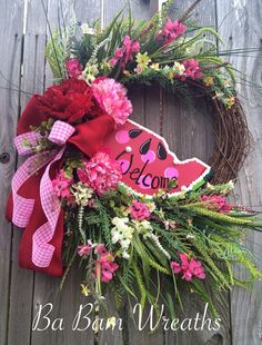 a wreath with pink flowers and red ribbon hanging on the side of a wooden fence