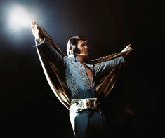 elvis presley performing on stage with his hands in the air and lights shining behind him