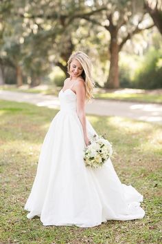 a woman in a white wedding dress holding a bouquet and posing for the camera with trees in the background