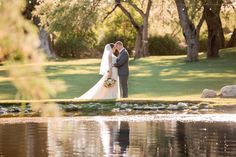 a bride and groom standing in front of a pond