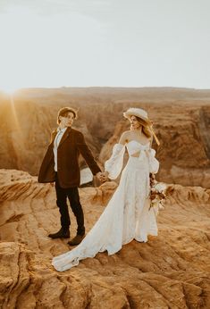 a bride and groom holding hands while standing on top of a cliff in the desert