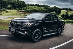 a black truck driving down the road under a cloudy sky with dark clouds in the background