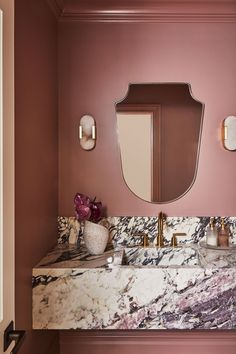 a bathroom with pink walls and marble counter tops, gold fixtures and mirrors on the wall