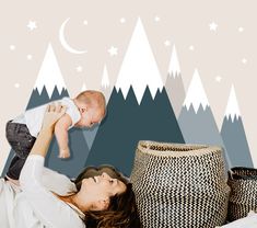 a woman holding a baby up in the air with mountains and stars behind her on a wall