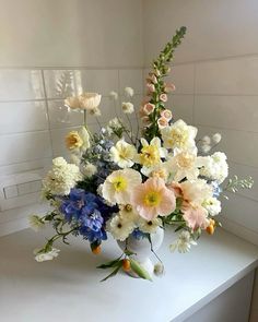 a white vase filled with lots of different colored flowers on top of a counter next to a window