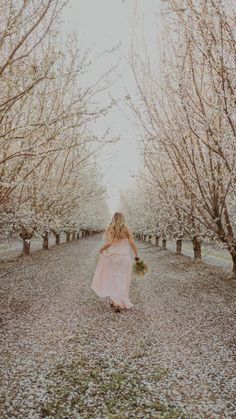 a woman in a pink dress walking through an orchard