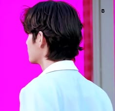 a man with black hair standing in front of a pink wall