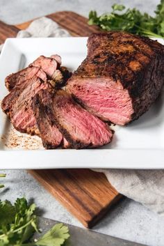 a piece of steak on a white plate with parsley next to it and a knife