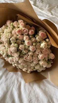 a bouquet of pink roses is wrapped in brown paper on a white bed linens