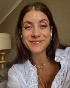 a smiling woman in a white shirt and gold necklace with an earring on her neck