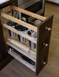 an open drawer with utensils and other kitchen items in it on a wooden floor