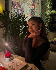 a woman sitting at a table in front of a cake with a candle on it