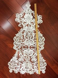 a white lace christmas tree on a wooden floor with a ruler in front of it