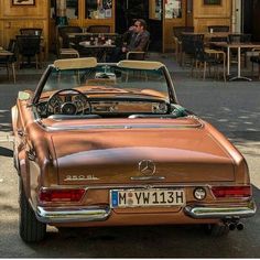 an old car is parked in front of a restaurant with people sitting at the tables