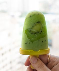 a hand holding an ice cream with a kiwi slice on it