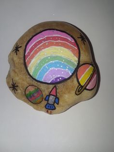 a rock with an image of a rocket, planets and a rainbow painted on it