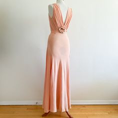 Vintage 1930s full length gown in drapey blush crepe with a subtle sheen, cut on the bias. Dress has a cowl neckline, diagonal seaming that drapes perfectly on the body, and a low back with pleating and a three dimensional flower at the center back crafted from crepe petals faced in pale green.  This piece captures all the glamour of the decade and is in great condition given its age and is in strong and very wearable shape. There are a few small holes in the skirt as shown and a few smaller pinhole sized ones; there is some darker spotting in areas and the hem could use a good cleaning but none of these are significant enough to detract from the gown itself.  This is either silk crepe or a high quality silk-like crepe woven. Looks to be an XS - shown on a dress form that is 34-24-35. Due Fitted Draped Bias Cut Maxi Dress, Fitted Bias Cut Draped Maxi Dress, Peach Fitted Floor-length Maxi Dress, Elegant Peach Maxi Dress For Evening, Old Hollywood Party, Silk Crepe Dress, Bias Dress, Glass Menagerie, 1930s Dress