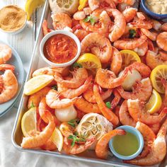 a tray filled with shrimp and lemons next to dipping sauce