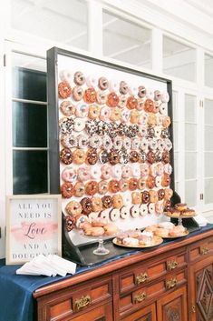 a table topped with lots of donuts on top of a wooden dresser next to a sign