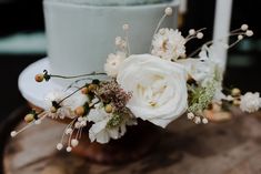 a cake with white flowers and greenery is on top of a wooden table next to candles