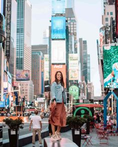 a woman standing on top of a bench in the middle of a city