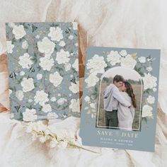 two wedding cards with flowers on them next to a white flowery background and the same photo