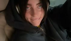 a woman wearing a hoodie is smiling for the camera while sitting in a car