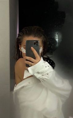 a woman taking a selfie in the mirror with her cell phone while wearing a white shirt