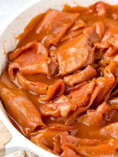 a white bowl filled with meat covered in gravy on top of a table