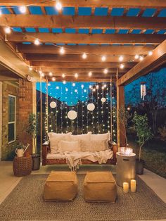 an outdoor living area with lights and pillows on the couches, in front of a pergolated patio