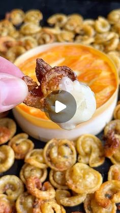 a person dipping some food into a bowl with pretzels in the foreground