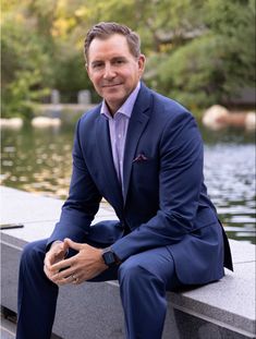 a man in a blue suit sitting on a ledge next to a body of water