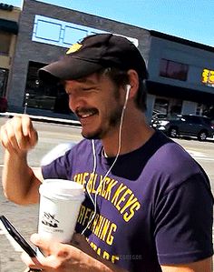 a man with headphones on is holding a cup and cell phone in his hand