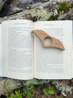 an open book with a wooden object stuck in it's cover, sitting on top of some moss