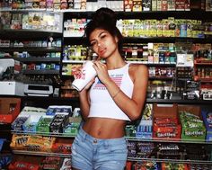 a woman standing in front of a grocery store holding a drink and chewing on a candy bar