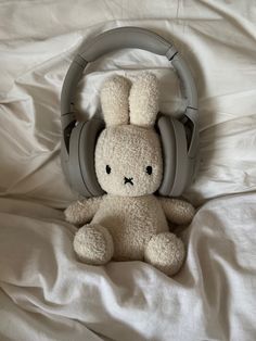 a stuffed animal with headphones on it's ears sitting on a white sheet