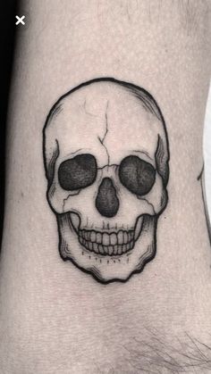 a black and white skull tattoo on the left arm, with two eyes drawn to it