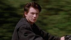 a young man riding on the back of a motorcycle in front of green grass and trees