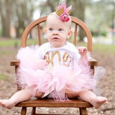 a baby sitting in a wooden chair wearing a pink tutu and a gold monogrammed shirt