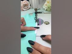 two hands are using a sewing machine to sew on some paper with black nail polish