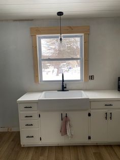 an empty kitchen with white cabinets and a window above the sink that is partially open